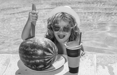 Kid boy hold watermelon relaxing in pool. Child swimming in water pool. Summer kids activity, watersports.の写真素材