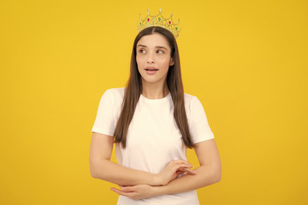 Pretty young woman wear crown, isolated on yellow color background. Girl with golden crown, arrogance and privileged status, concept of success and dreams.の写真素材