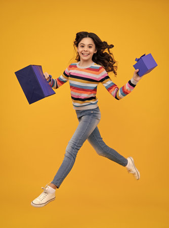 Girl teenager with shopping bags isolated on yellow backgound. Shopping and sale concept. Run and jump.の写真素材