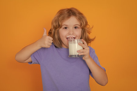 Healthy drink with calcium and protein for kids. Funny blonde child drinking milk isolated on yellow. Little boy with milk mustache hold glass of milk.の写真素材