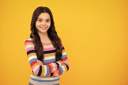 Cute little teenager girl crossing arms over yellow background. Copy space. Happy teenager, positive and smiling emotions of teen girl.の写真素材