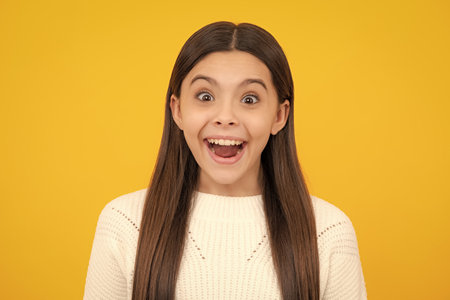 Excited face. Amazed expression, cheerful and glad. Close up portrait of caucasian teen girl. Head shot of cute teenager child on yellow isolated studio background.の写真素材