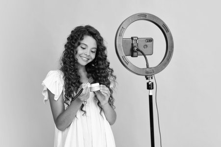 Teen girl blogger influencer use selfie led lamp and smartphone on tripod for making online video tutorial. Teenager vlogger making vlog for kids channel. Positive and smiling emotions of teen girl.の写真素材