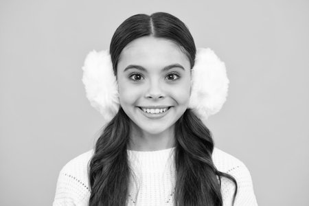 Beautiful winter kids portrait. Teenager girl posing with winter sweater and winter warm earmuff ear-flaps on yellow background. Happy face, positive and smiling emotions of teenager girl.の写真素材