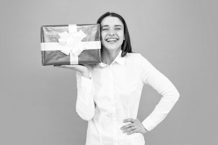Portrait of a happy girl with gift box isolated over gray background. Woman holding gift present.の写真素材