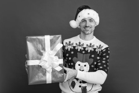Portrait of Santa man in sweater holding big red present box isolated over red background. Concept of x-mas time celebration holidays, happiness, emotions.の写真素材
