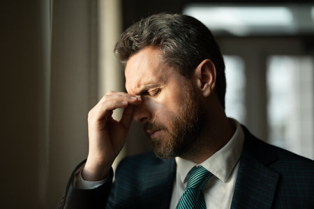 Tired man having a terrible headache. Exhausted man feeling unhealthy, upset about headache illness. Stressed middle-aged man having headache. Migraine and headache concept.の写真素材