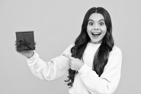 Happy face, positive and smiling emotions of teenager girl. Teenager child holding gift box on yellow isolated background. Gift for kids birthday. Christmas or New Year present box.の写真素材