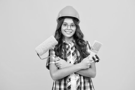 Teenager child painter in helmet with painting brush. Child in hard hat. Kid builder painter on construction site. Renovation and repair.の写真素材