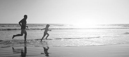 Silhouette of father and son run on summer beach outdoor, banner poster with copy space. daddy with kid boy in sea or ocean. weekend family day.の写真素材