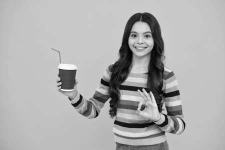 Child with coffee or tea cup isolated on yellow studio background. Teenage girl with take away beverage. Happy teenager, positive and smiling emotions of teen girl.の写真素材
