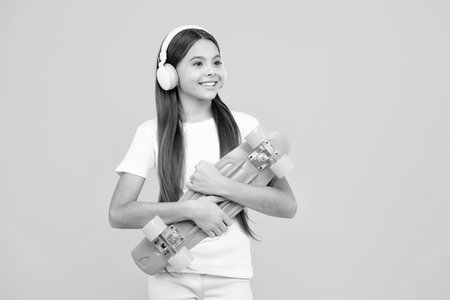 Happy teenager portrait. Teen hipster girl skater with skateboard and headphones on isolated background. Summer kids trend, urban teenage style. Smiling girl.の写真素材