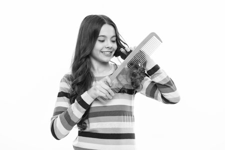 Child brushing combing hair with big comb on white isolated studio background. Teen girl with hairbrush. Kids hairstyle. Happy girl face, positive and smiling emotions.の写真素材