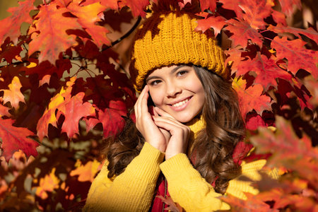 cheerful girl in hat standing at autumn leavesの写真素材