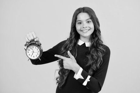 Teen student girl with clock isolated on yellow background. Child back to school. Education and time concept.の写真素材