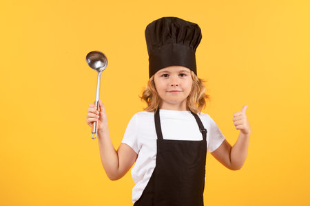 Funny kid chef cook with kitchen ladle, studio portrait. Cooking children. Chef kid boy making healthy food. Portrait of little child in chef hat isolated on studio background. Kid chef.の写真素材