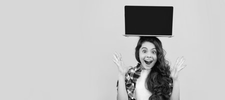 amazed smart kid with laptop on head presenting school online lesson, elearning. School girl portrait with laptop, horizontal poster. Banner header with copy space.の写真素材