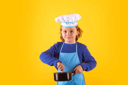 Kid chef cook with cooking pot stockpot. Chef kid boy making healthy food. Portrait of little child in chef hat isolated on studio background. Child chef. Cooking process.の写真素材