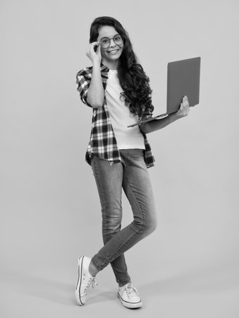 Student school girl with laptop on isolated studio background. Video online webinar, learn on laptop, elearning lesson, pc computer call. Happy teenager, positive and smiling schoolgirl.の写真素材