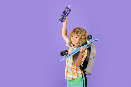 Kid with skateboard and water bottle on violet studio background. Child hold skate board. Healthy sport and activity for school kids in summer. Sports fun.の写真素材