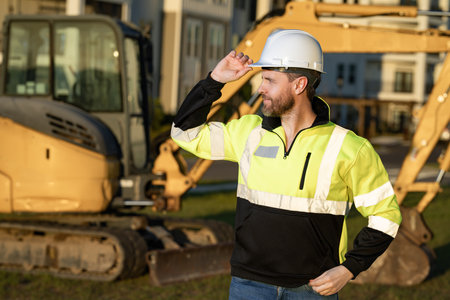 Worker at construction site. Builder in hardhat. Construction man with helmet. Worker at construction with helmet. Industry worker at construction building. Builder at site building with excavator.の写真素材