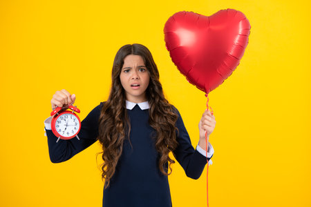 Angry teenager girl, upset and unhappy negative emotion of teen student girl with clock isolated on yellow background. Child back to school. Education and time concept.の写真素材