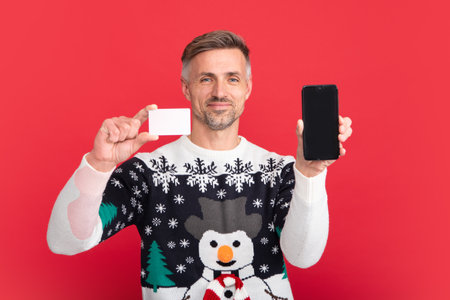 Man with phone and credit card. Man in Christmas sweater and Santa hat on red background.の写真素材