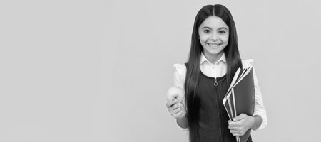 Happy kid back to school holding apple and books yellow background. Portrait of schoolgirl student, studio banner header. School child face, copyspace.の写真素材