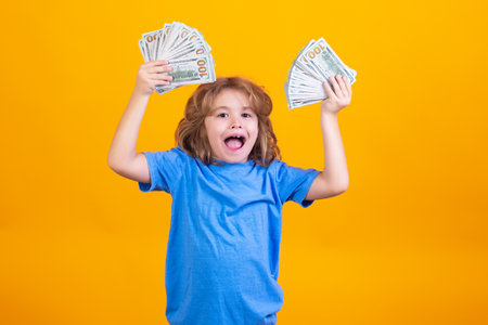 Money win, big luck. Child with lots of money dollar banknotes isolated over yellow studio background.の写真素材