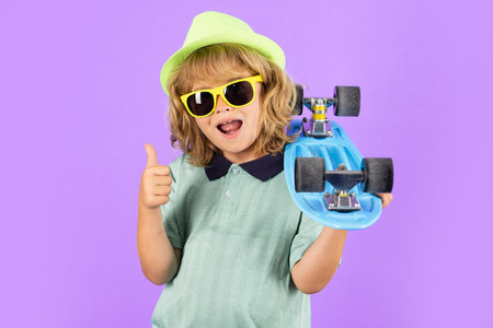 Happy child boy holding skateboard over blue background isolated. Studio portrait of fashion kids.の写真素材