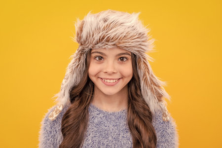 happy teen girl wear earflap hat on yellow background, winter clothingの写真素材