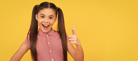 Happy girl child point finger gun hand gesture yellow background, pointing. Child face, horizontal poster, teenager girl isolated portrait, banner with copy space.の写真素材