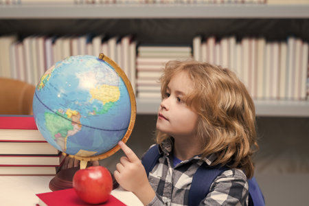 Pupil looking at globe in library at the elementary school. Nerd school kid. Clever child from...