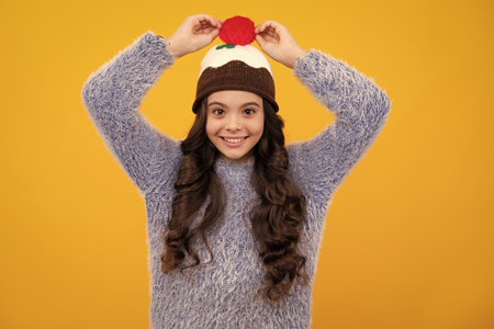 Modern teen girl wearing sweater and knitted hat on isolated yellow background. Happy teenager, positive and smiling emotions of teen girl.の写真素材