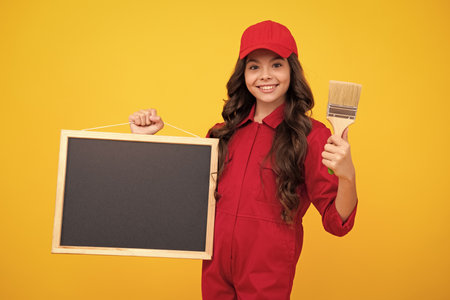 Painter with painting brush tool or paint roller hold blackboard. Worker isolated on yellow background. Kids renovation concept. Happy face, positive and smiling emotions of teenager girl.の写真素材