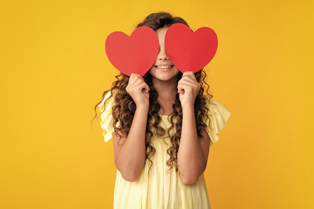 Happy teenager portrait. Cheerful lovely romantic teen girl hold red heart symbol of love for valentines day isolated on yellow background. Smiling girl.の写真素材