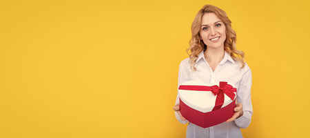 happy woman hold present heart box on yellow background. Woman isolated face portrait, banner with mock up copy space.の写真素材