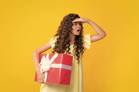 Teenager child holding gift box on yellow isolated background. Gift for kids birthday. Christmas or New Year present box. Excited teenager, glad amazed and overjoyed emotions.の写真素材