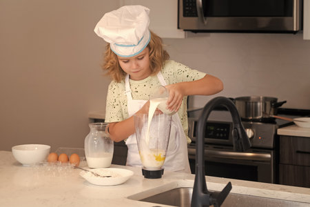 Fun kids kitchen. Funny little kid chef cook wearing uniform cook cap and apron cooked food in the kitchen. Kids are preparing food, bake cookies in the kitchen.の写真素材