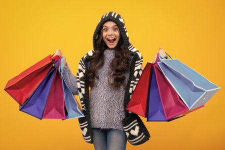 Winter shopping sale. Amazed teenager. Child girl hold shopping bag enjoying sale isolated on yellow background. Portrait of teenager girl is ready to go shopping. Excited teen girl.の写真素材
