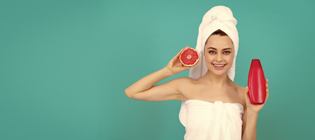 happy beautiful woman in towel with grapefruit shampoo bottle on blue background. Beautiful woman isolated face portrait, banner with mock up copy space.の写真素材