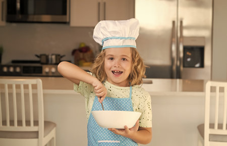 Child chef cook with cooking plate. Fun kids kitchen. Funny little kid chef cook wearing uniform cook cap and apron cooked food in the kitchen. Kids are preparing food, bake cookies in the kitchen.の写真素材