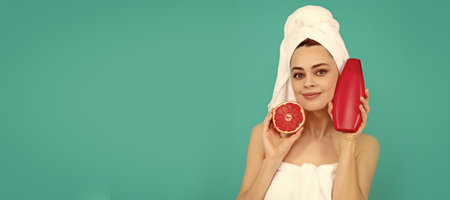 smiling woman in towel with grapefruit shampoo bottle on blue background. Beautiful woman isolated face portrait, banner with mock up copy space.の写真素材
