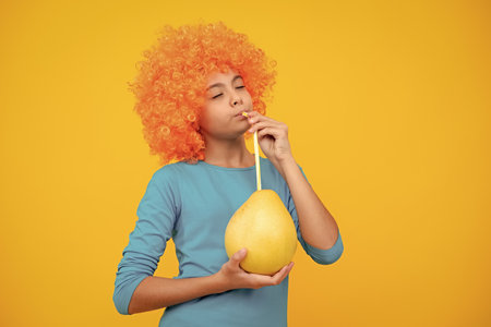 Summer fruits. Teenager child girl hold citrus fruit pummelo or pomelo, isolated on yellow background. Kid healthy eating.の写真素材