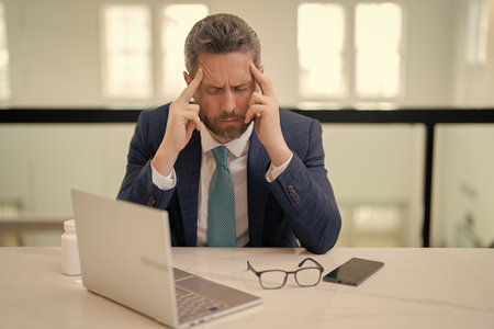 Overworked burnout man feeling migraine head strain. Tired bored business man has office syndrome. Exhausted man with migraine or headache. Office worker, manager or freelancer having a headache.の写真素材