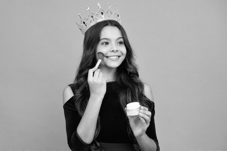 Child teen girl making beauty make up, hold powder and brush. Beautiful teenager applying makeup with powder. Happy face, positive and smiling emotions of teenager girl.の写真素材