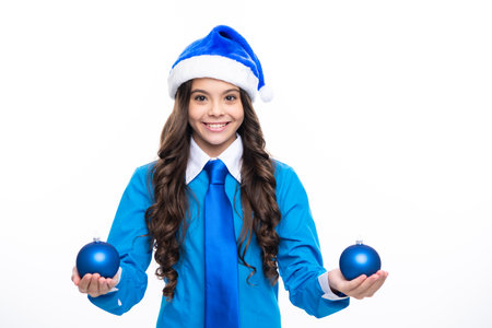 Christmas kids, New Year celebration concept. Portrait a teenage girl child 12, 13, 14 years old with blue santa hat, shirt and necktie hold christmas ball isolated on white background.の写真素材