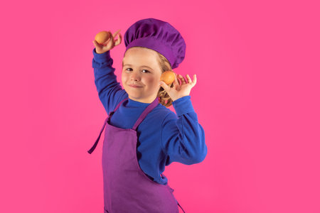 Child cook hold eggs. Kid chef cook prepares food on isolated studio background. Kids cooking. Teen boy with apron and chef hat preparing a healthy meal.の写真素材