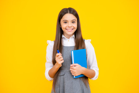 Back to school. Teenager schoolgirl with book ready to learn. School girl children on isolated yellow studio background.の写真素材