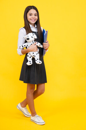 Schoolgirl 12, 13, 14 years old with toy. School children cuddling favorite toys on yellow background. Happy childhood. Happy girl face, positive and smiling emotions.の写真素材